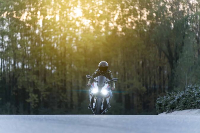 Man driving a big motorbike on an empty road Man driving a big motorbike on an empty road with lights on and sunset on the background with some tall trees