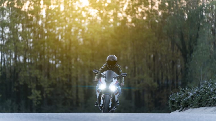 Man driving a big motorbike on an empty road Man driving a big motorbike on an empty road with lights on and sunset on the background with some tall trees